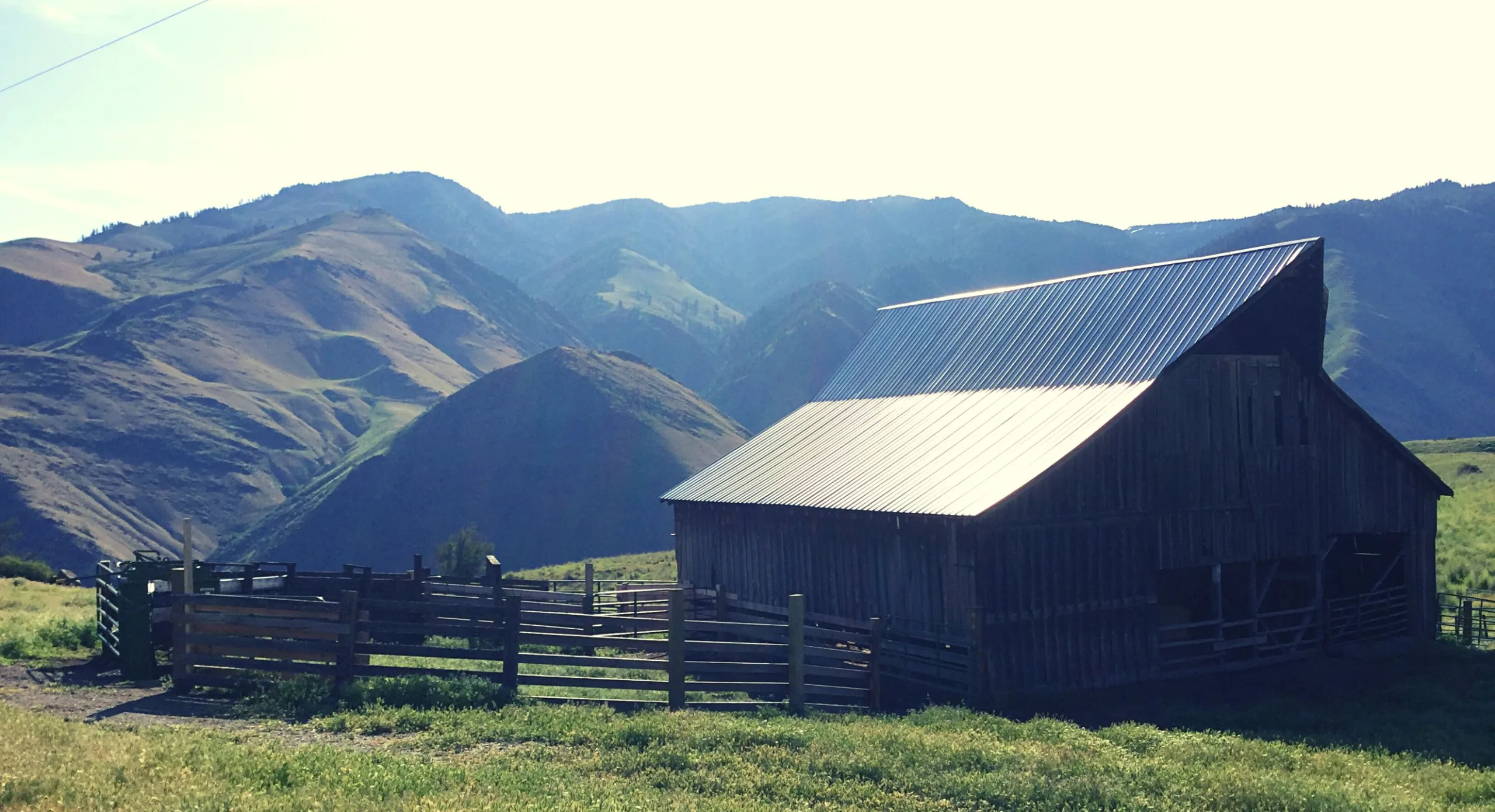 A weathered barn and stock corrals on a ranch above the Salmon River breaks, backlit ridgelines behind.